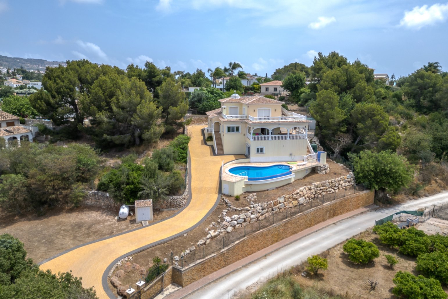Vue aérienne de la villa sur plusieurs niveaux avec piscine à débordement, vastes terrasses et allée privée, entourée de pins et de murs en pierre.