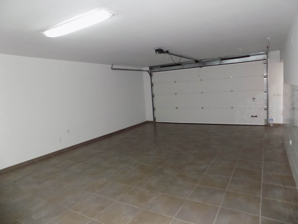 Grand garage double en sous-sol avec revêtement de sol en grès cérame, murs blancs et porte sectionnelle automatique motorisée.