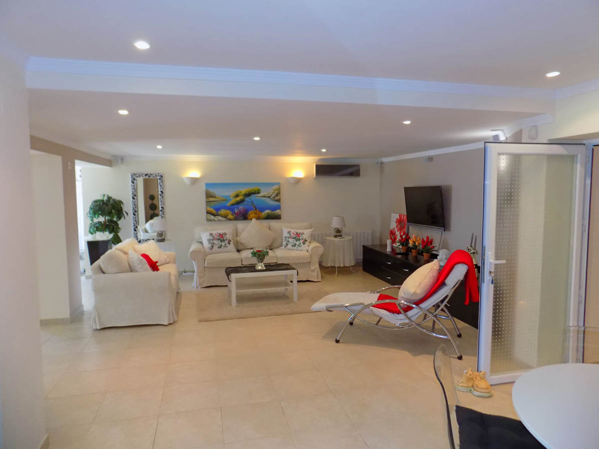 Grand salon au rez-de-chaussée avec carrelage clair, éclairage encastré au plafond et porte vitrée donnant sur l'espace extérieur.