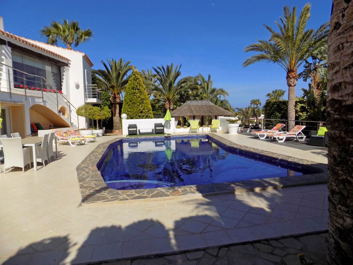 Piscine extérieure bordée de pierre, vaste terrasse carrelée avec coin repas, transats et pavillon de détente au cœur d'un jardin méditerranéen.