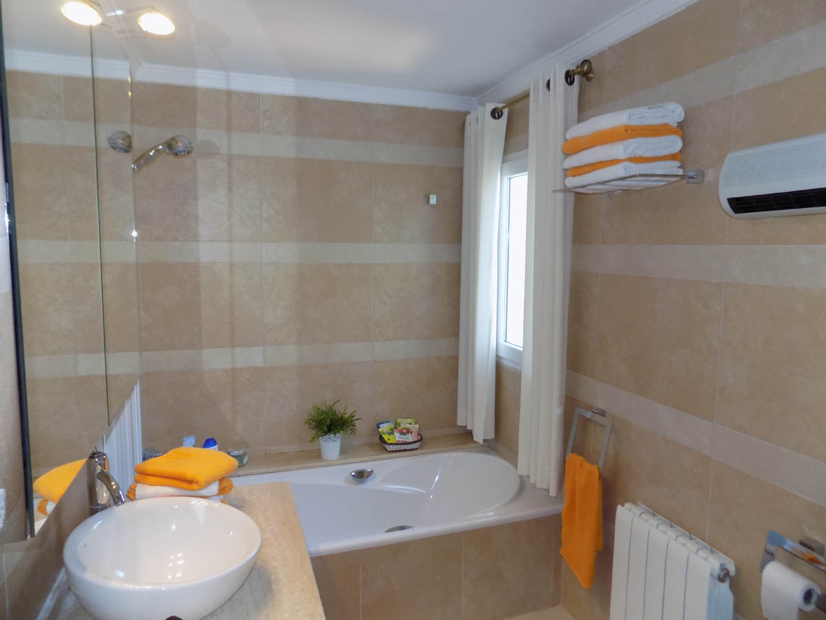 Salle de bain avec baignoire encastrée, vasque à poser sur plan de travail en pierre et murs revêtus de carreaux beiges aux bandes horizontales.
