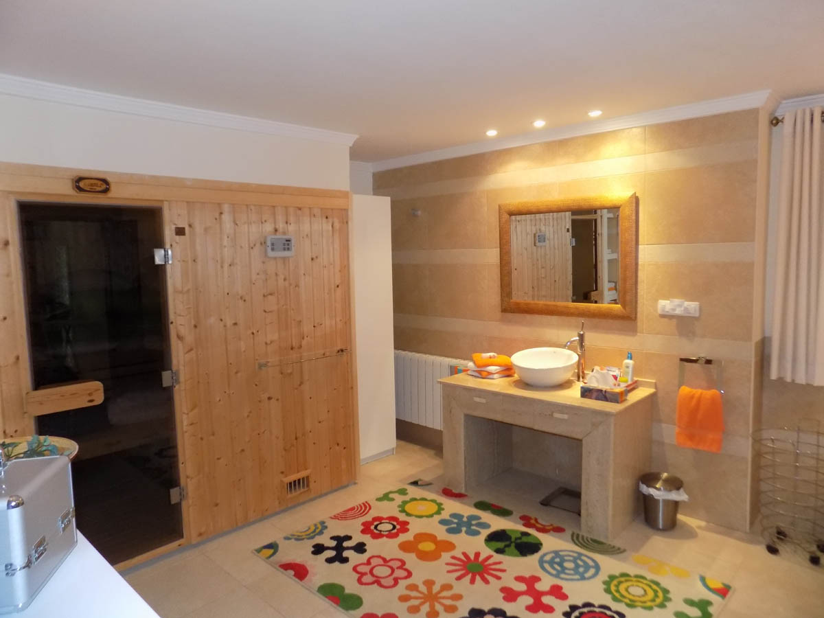 Salle de bain avec sauna en bois intégré, meuble vasque en pierre naturelle et carrelage mural aux tons chauds. Éclairage encastré et radiateur installés.