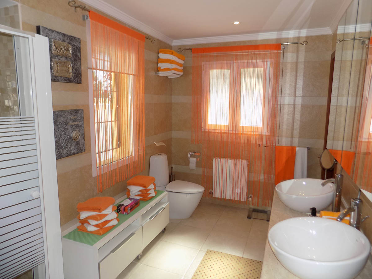 Salle de bain complète avec double vasque à poser, carrelage mural aux tons beiges et lumière naturelle abondante grâce aux fenêtres.