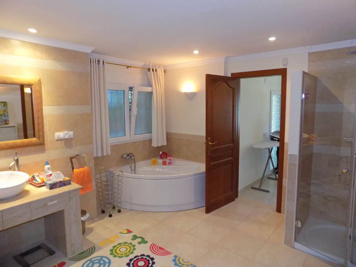 Salle de bains avec baignoire balnéo d'angle, douche à l'italienne et plan de toilette en pierre avec vasque à poser et éclairage encastré.