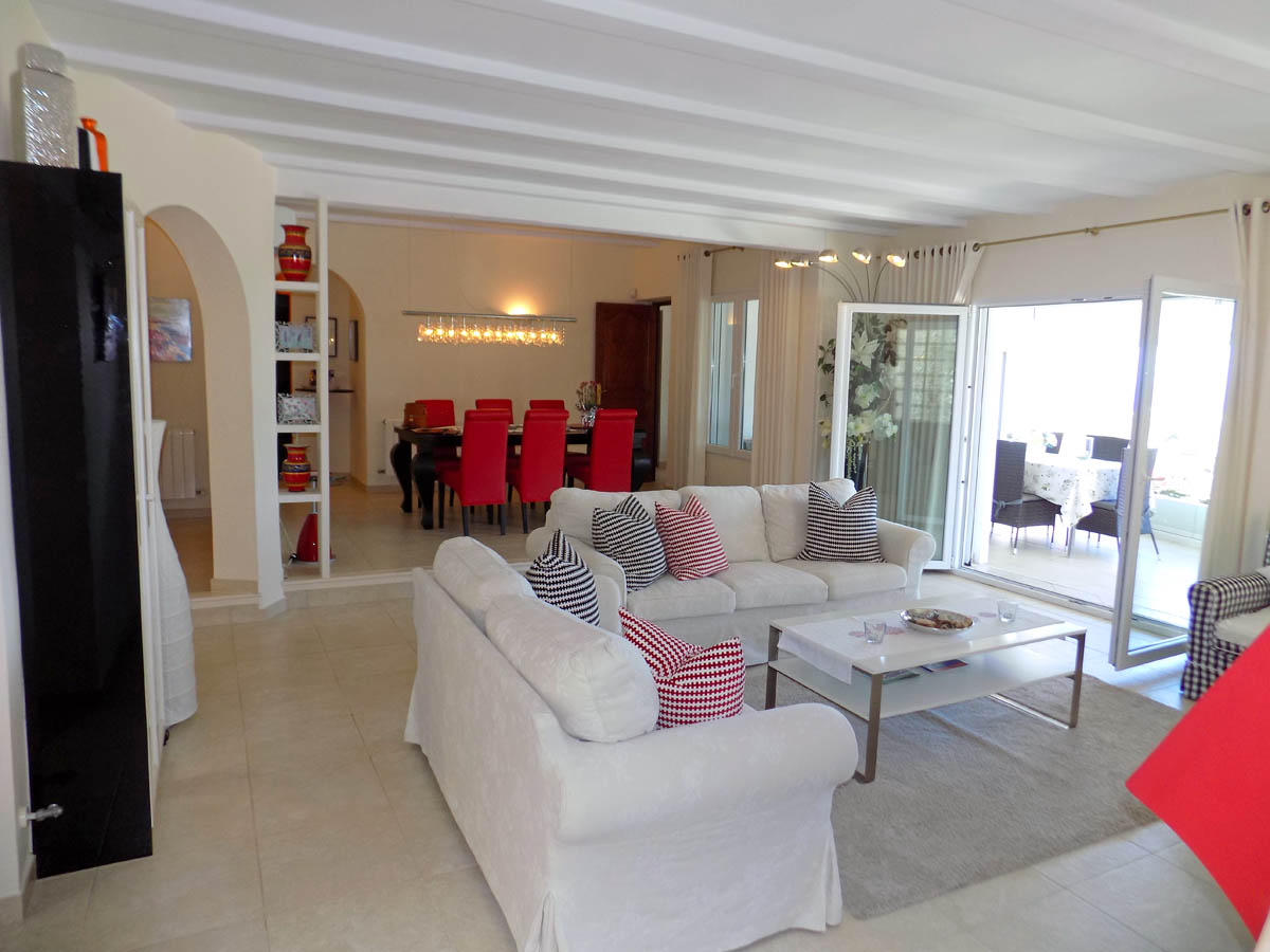 Salon et salle à manger à aire ouverte avec plafonds à poutres blanches, carrelage au sol et accès direct à la terrasse par de grandes portes vitrées.
