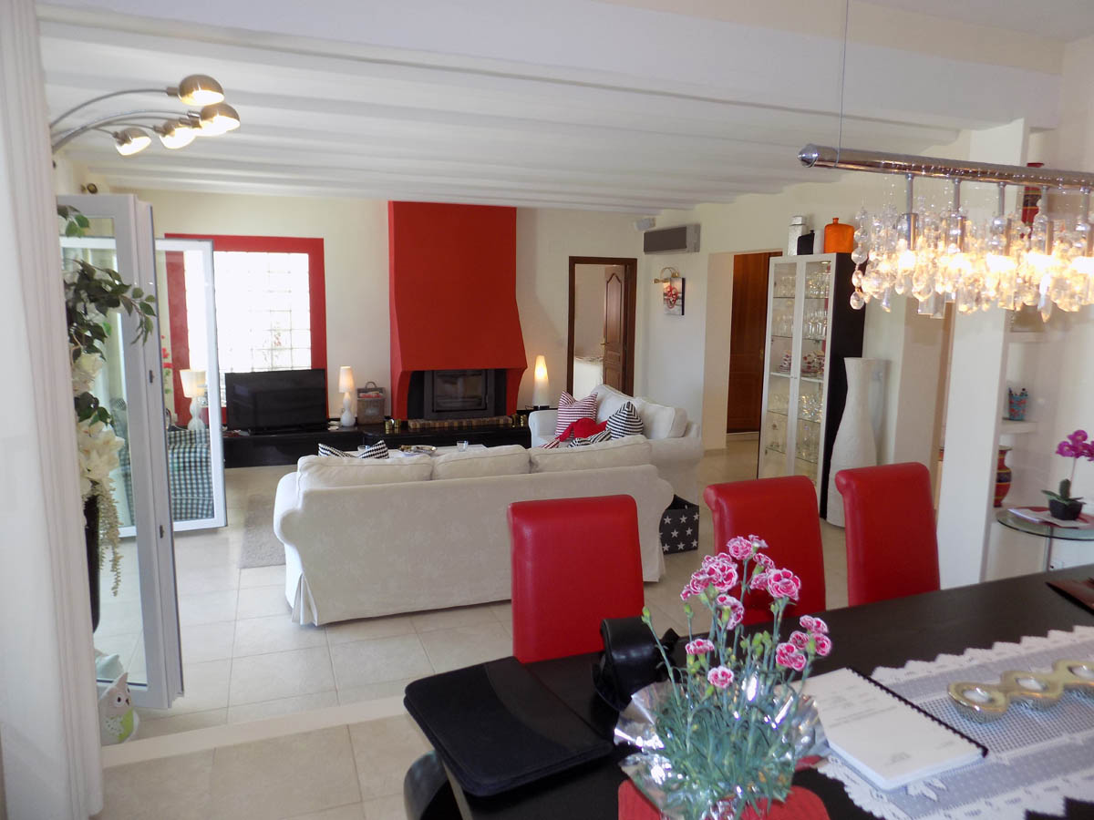 Salon-salle à manger à aire ouverte avec une cheminée rouge distinctive, des plafonds à poutres blanches et un mobilier élégant aux accents rouges.