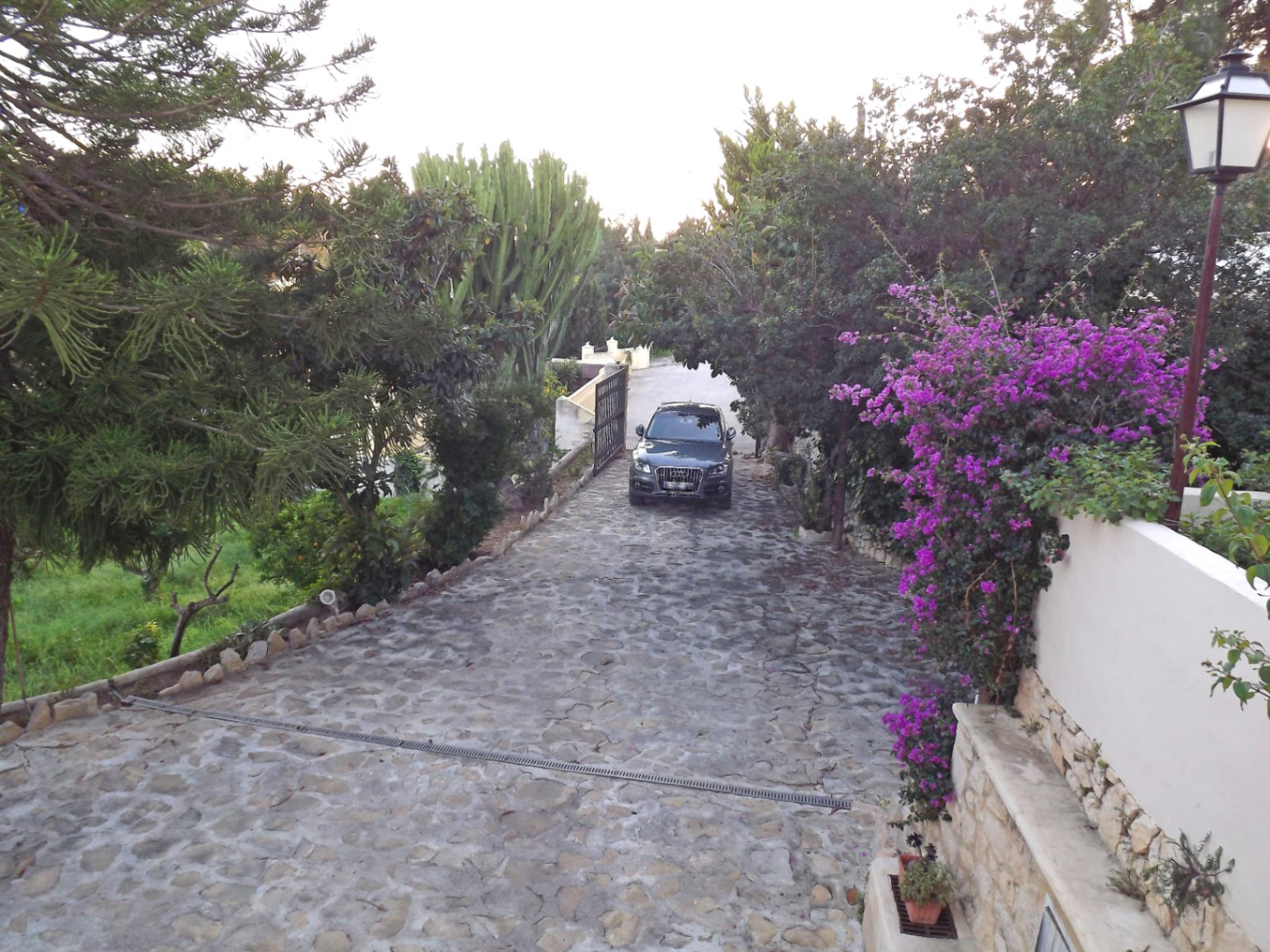 Allée privée pavée de pierres naturelles, bordée d'une végétation méditerranéenne luxuriante, de bougainvilliers et d'un mur d'enceinte en pierre et crépi blanc.
