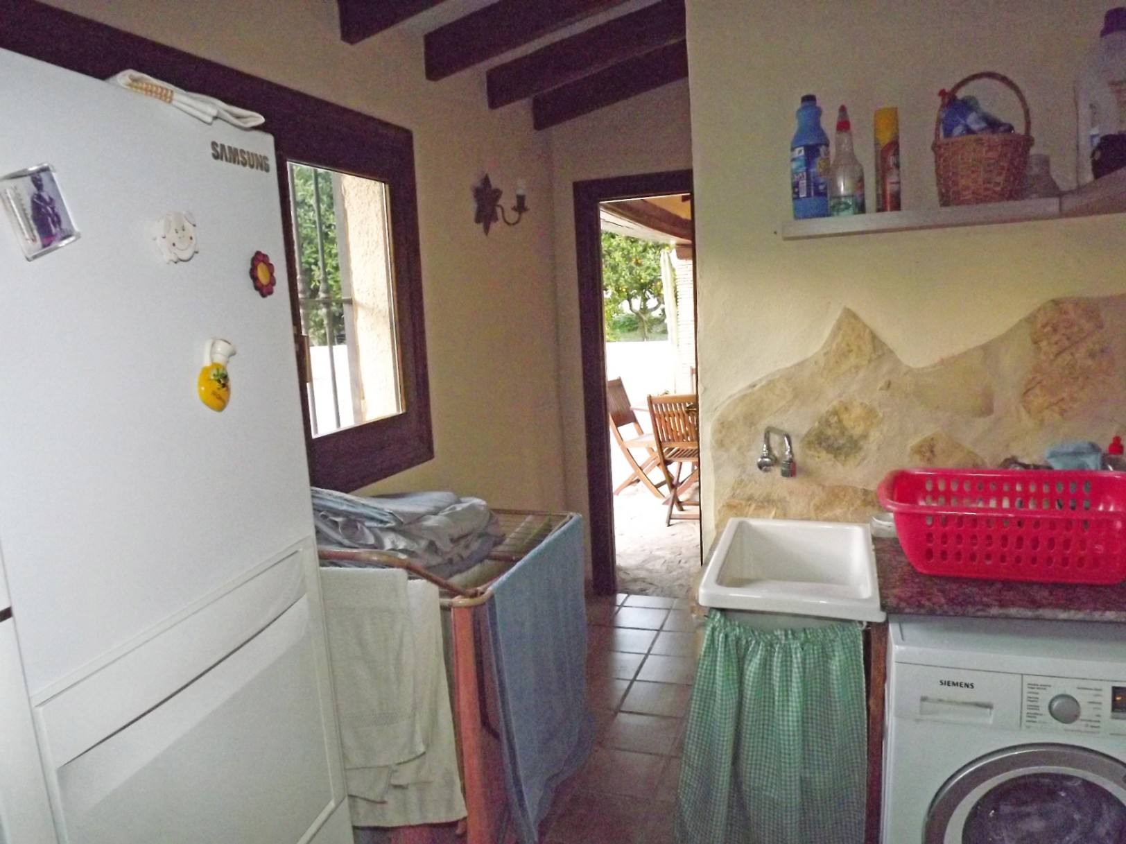 Buanderie fonctionnelle avec poutres en bois apparentes, lave-linge Siemens et accès direct à la terrasse. Présente des détails muraux en pierre naturelle.