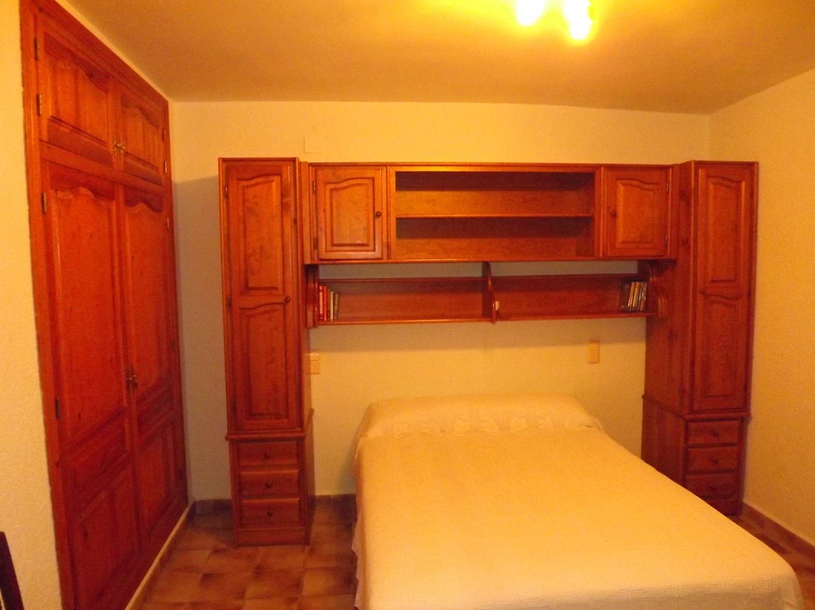 Chambre avec mobilier en bois massif, comprenant une armoire encastrée et un pont de lit avec étagères et rangements intégrés.