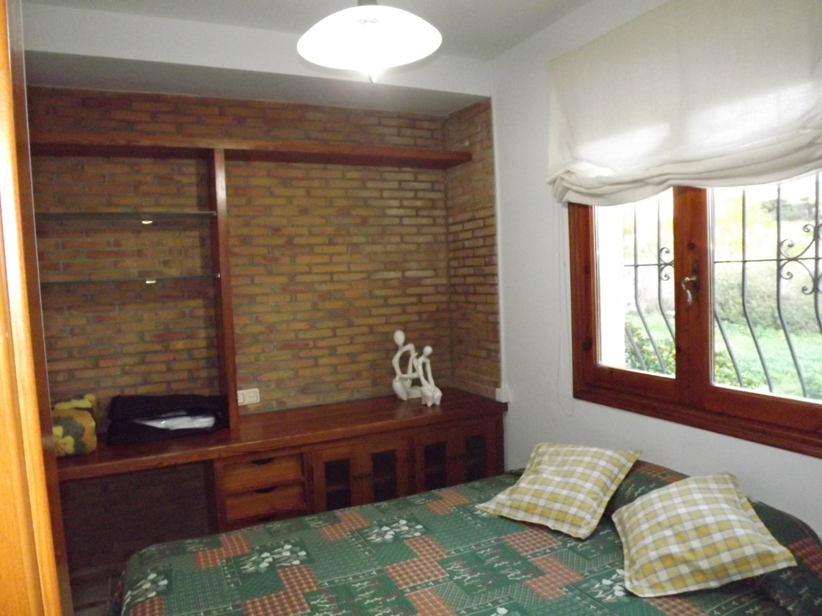 Chambre avec un mur en briques apparentes, des meubles en bois intégrés avec étagères en verre et une fenêtre en bois offrant une vue sur le jardin.