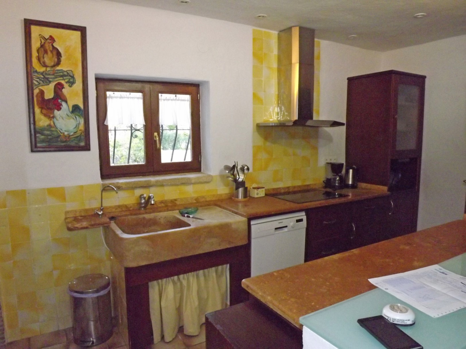 Cuisine de style rustique avec évier en pierre naturelle, crédence en carreaux jaunes, meubles en bois sombre et plan de travail en marbre sous spots encastrés.