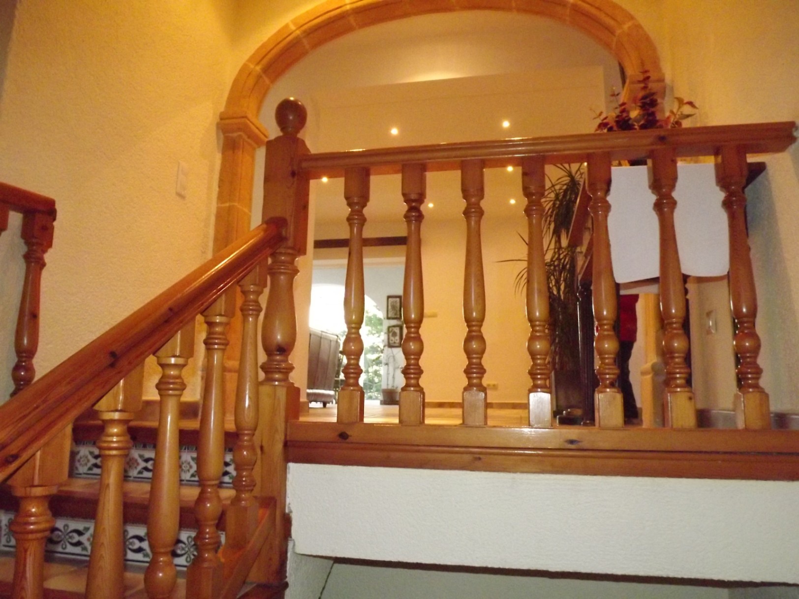 Escalier intérieur avec balustrade en bois tourné, contremarches en carrelage décoratif et arche en pierre naturelle menant au palier supérieur.