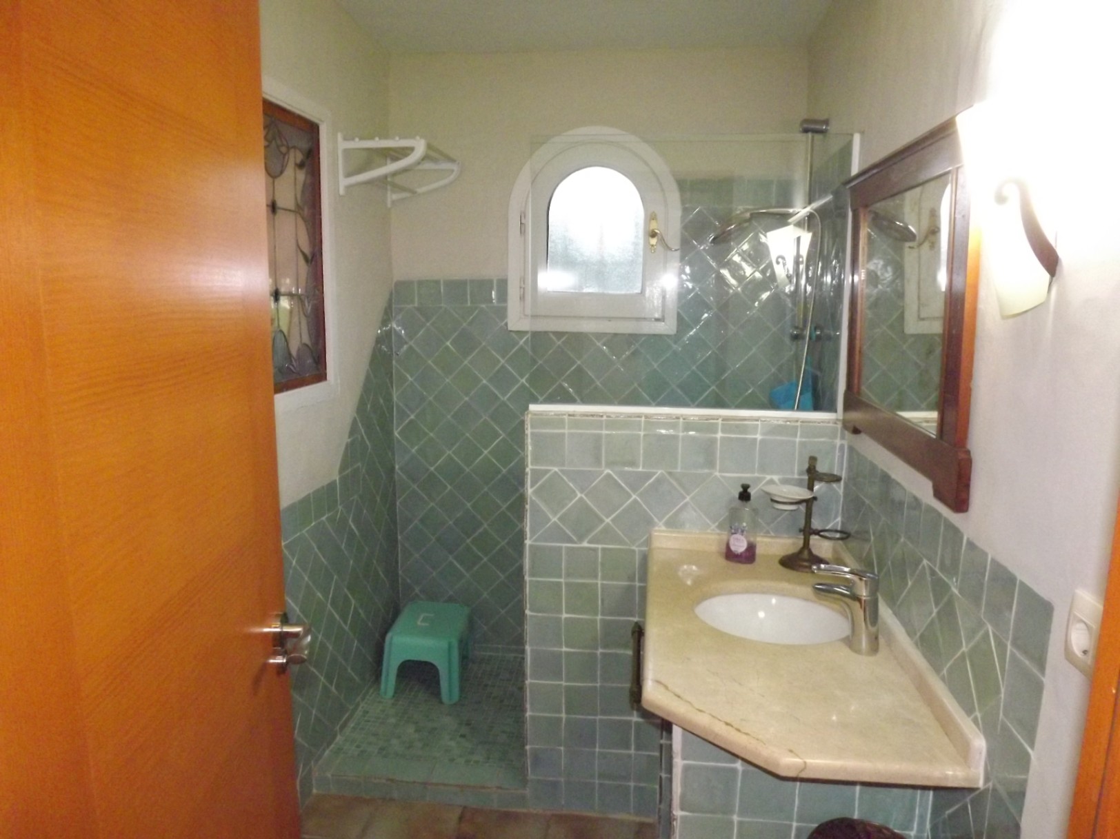 Salle de bain avec carrelage vert en diagonale, plan de toilette en marbre et douche à l'italienne avec fenêtre en plein cintre.