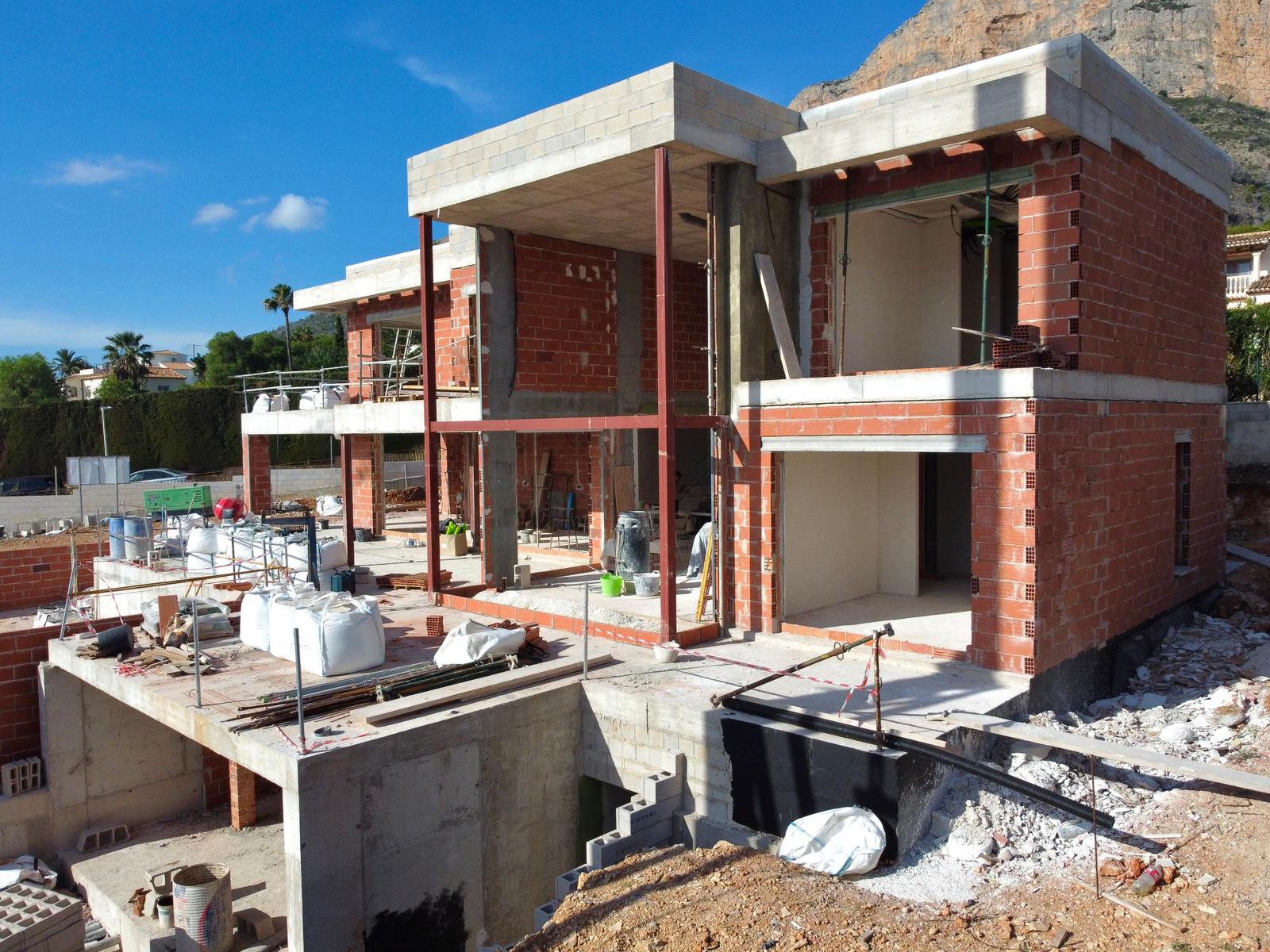 État actuel de la construction de la villa, montrant la structure en briques, les dalles en béton et les poutres en acier avec le Montgó en arrière-plan.