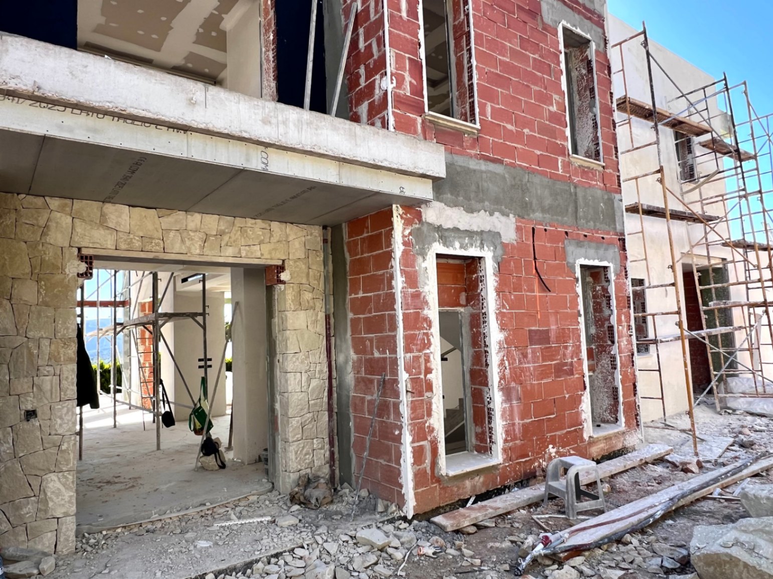 État actuel de la construction montrant la façade en briques, le revêtement en pierre naturelle et la structure en béton avec échafaudages extérieurs.
