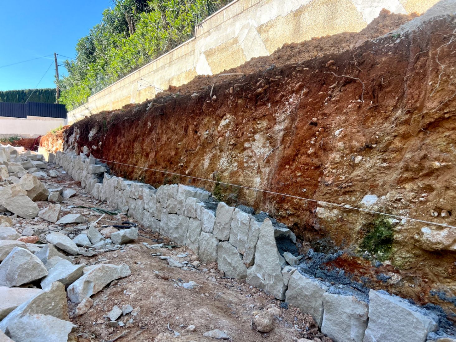 Phase initiale de construction montrant l'édification d'un mur de soutènement en pierre naturelle sur le terrain excavé.