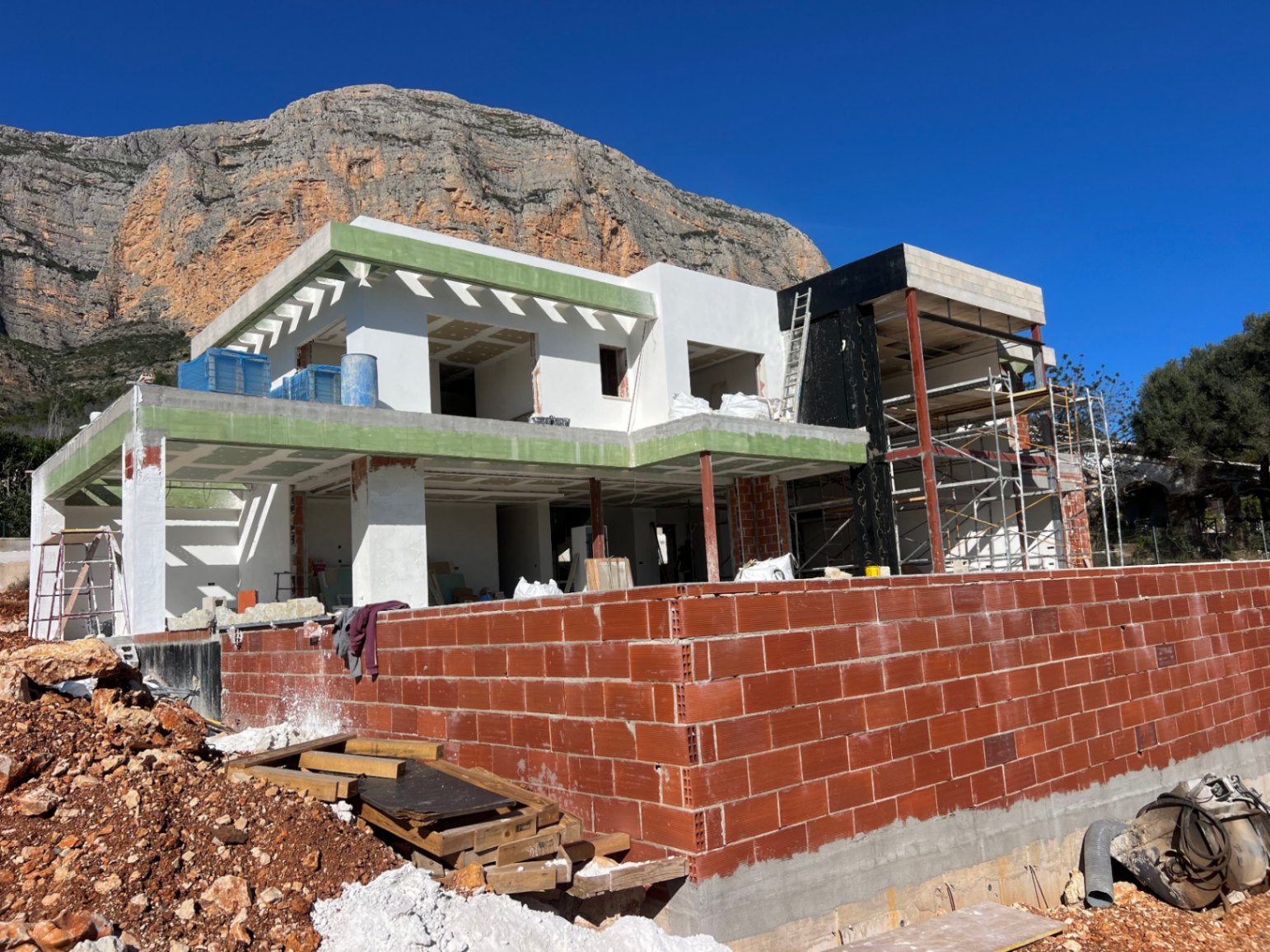 Vue extérieure de la villa en cours de construction devant le Montgó, mettant en valeur la structure sur deux niveaux et les vastes espaces terrasses.