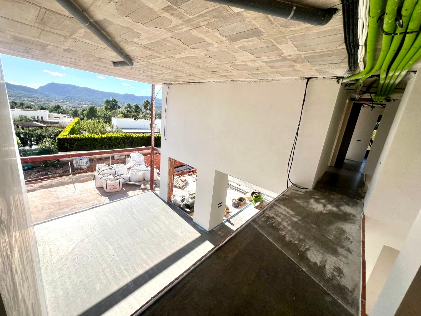 Vue intérieure de l'étage supérieur en chantier, montrant le plafond en béton, les gaines électriques et une vue dégagée sur la vallée et les montagnes de Jávea.
