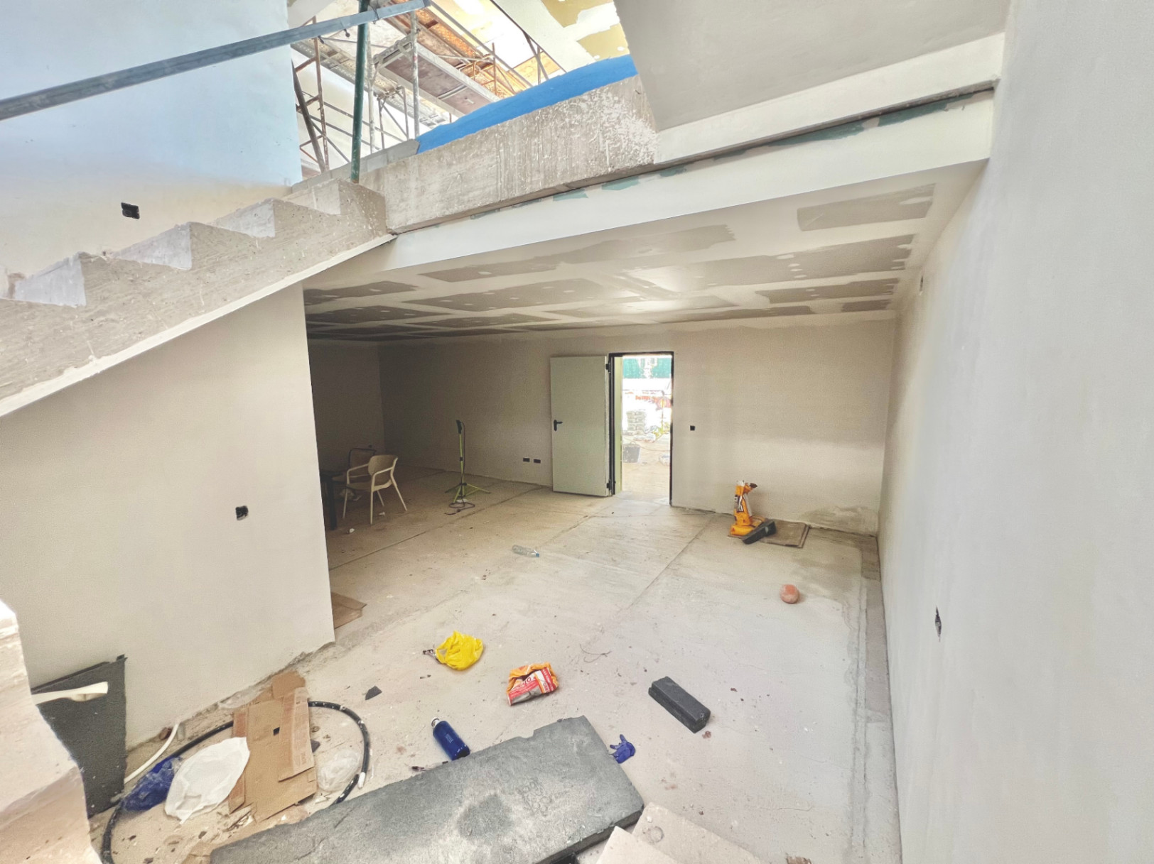 Vue intérieure du niveau inférieur en construction, présentant l'escalier en béton et un espace ouvert destiné à une salle de sport ou de cinéma.