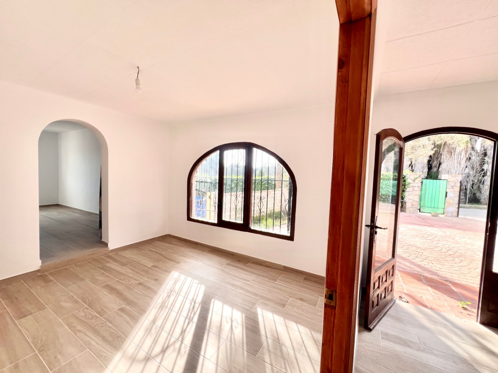 Espace de vie lumineux avec sol en grès cérame imitation bois, fenêtres cintrées en bois sombre et accès direct à la cour pavée.