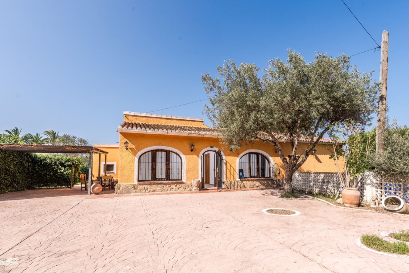 Façade ocre avec fenêtres cintrées et soubassement en pierre. L'extérieur offre une vaste cour pavée agrémentée d'un olivier mature et d'une pergola latérale.