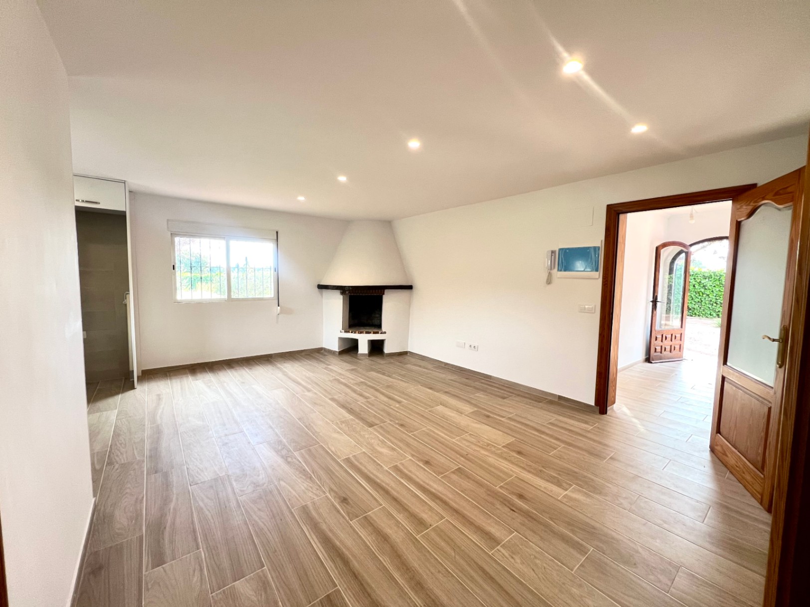 Salon spacieux avec cheminée d'angle, spots encastrés au plafond et sol en grès cérame imitation bois. La pièce communique avec l'entrée par des encadrements en bois massif.