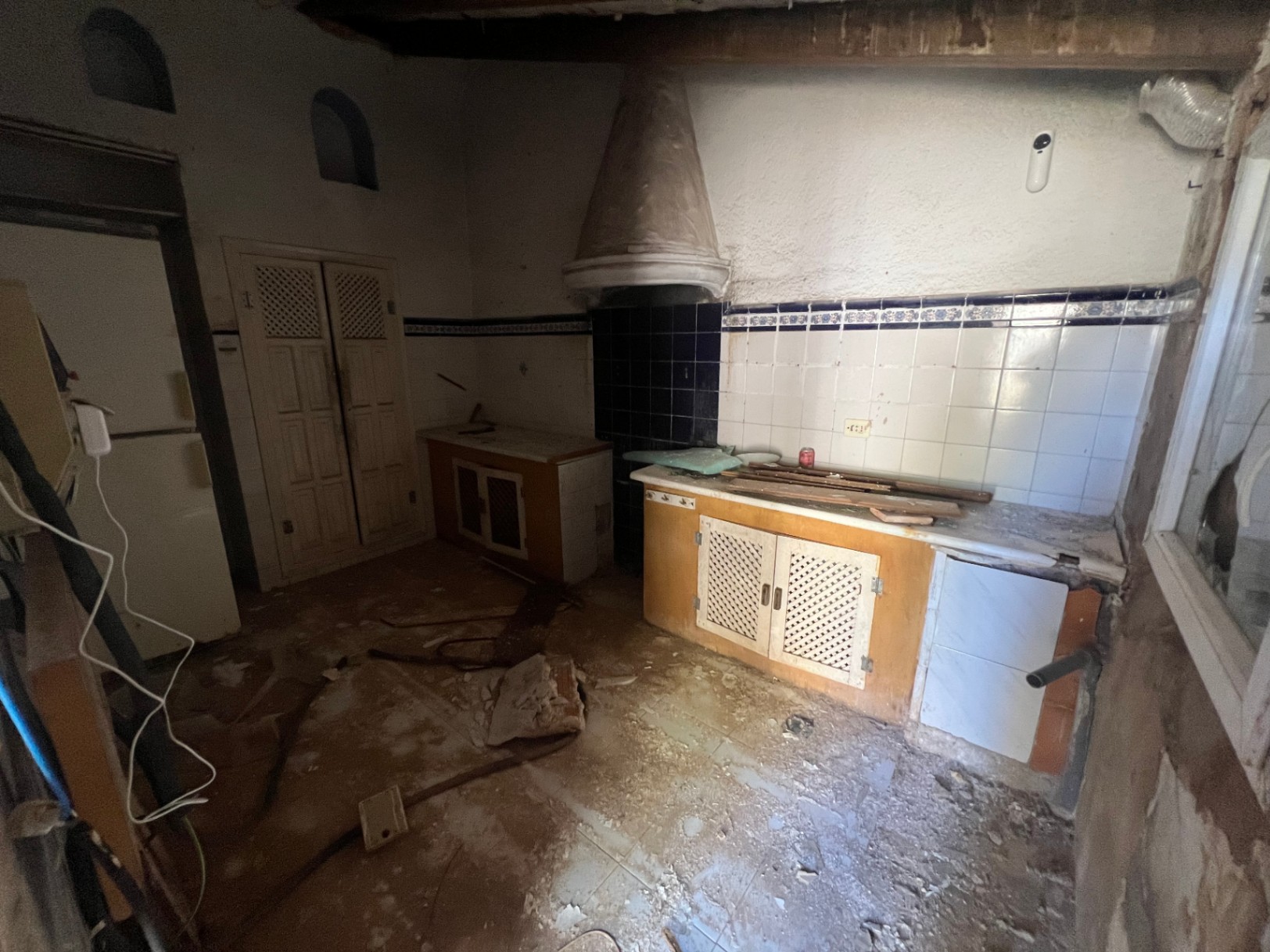 Cuisine d'origine à rénover avec hotte aspirante conique, crédence en carrelage blanc à liseré bleu et meubles en bois avec portes à treillis traditionnelles.