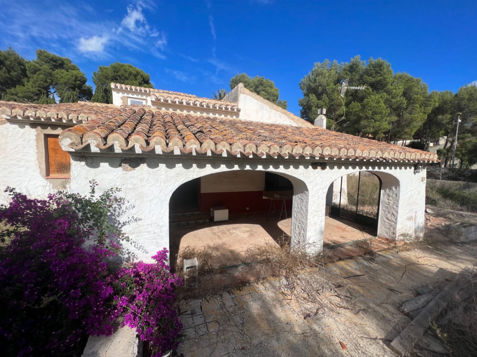 Façade extérieure avec une naya traditionnelle à arches et toiture en tuiles. Cette structure méditerranéenne est entourée de végétation et nécessite une rénovation.
