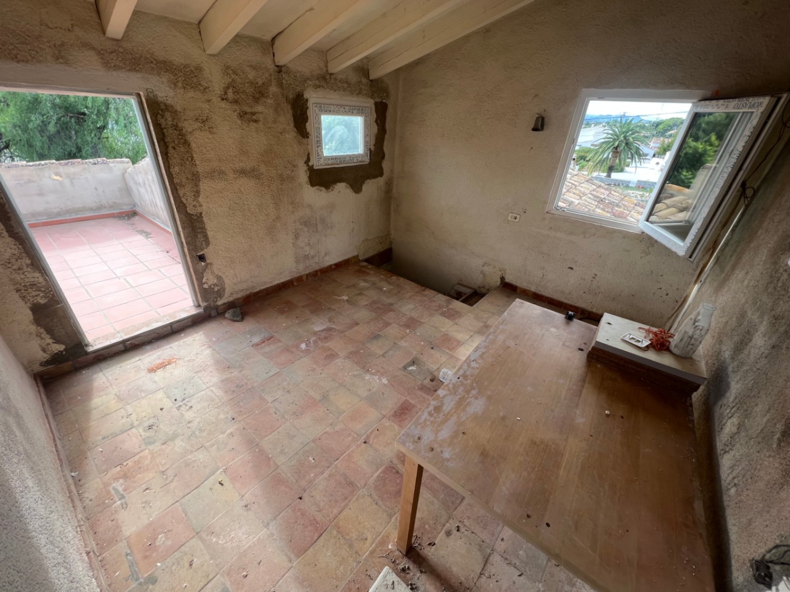 Pièce à l'étage à rénover avec poutres apparentes, sol en terre cuite et accès à une terrasse privée offrant une vue sur les environs.