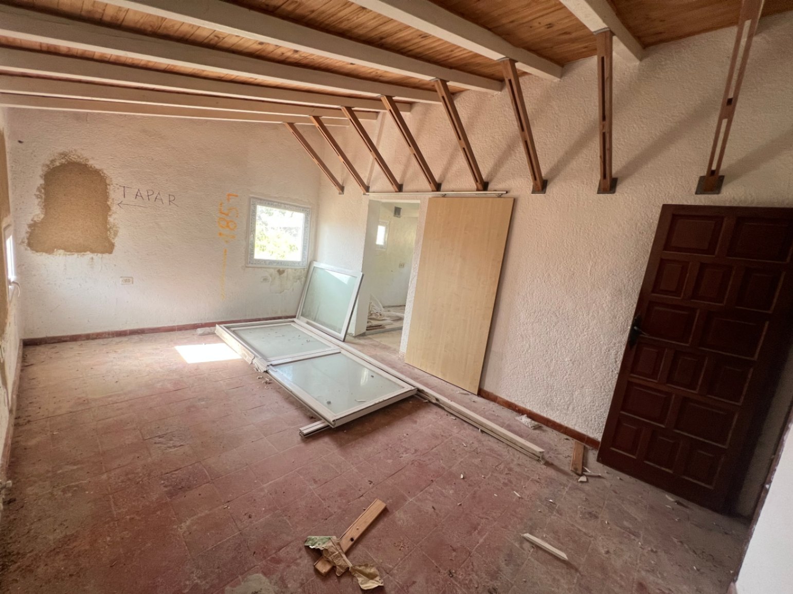Pièce à rénover avec plafonds à poutres apparentes en bois, sol en terre cuite et murs texturés. Un espace brut offrant de nombreuses possibilités d'aménagement.