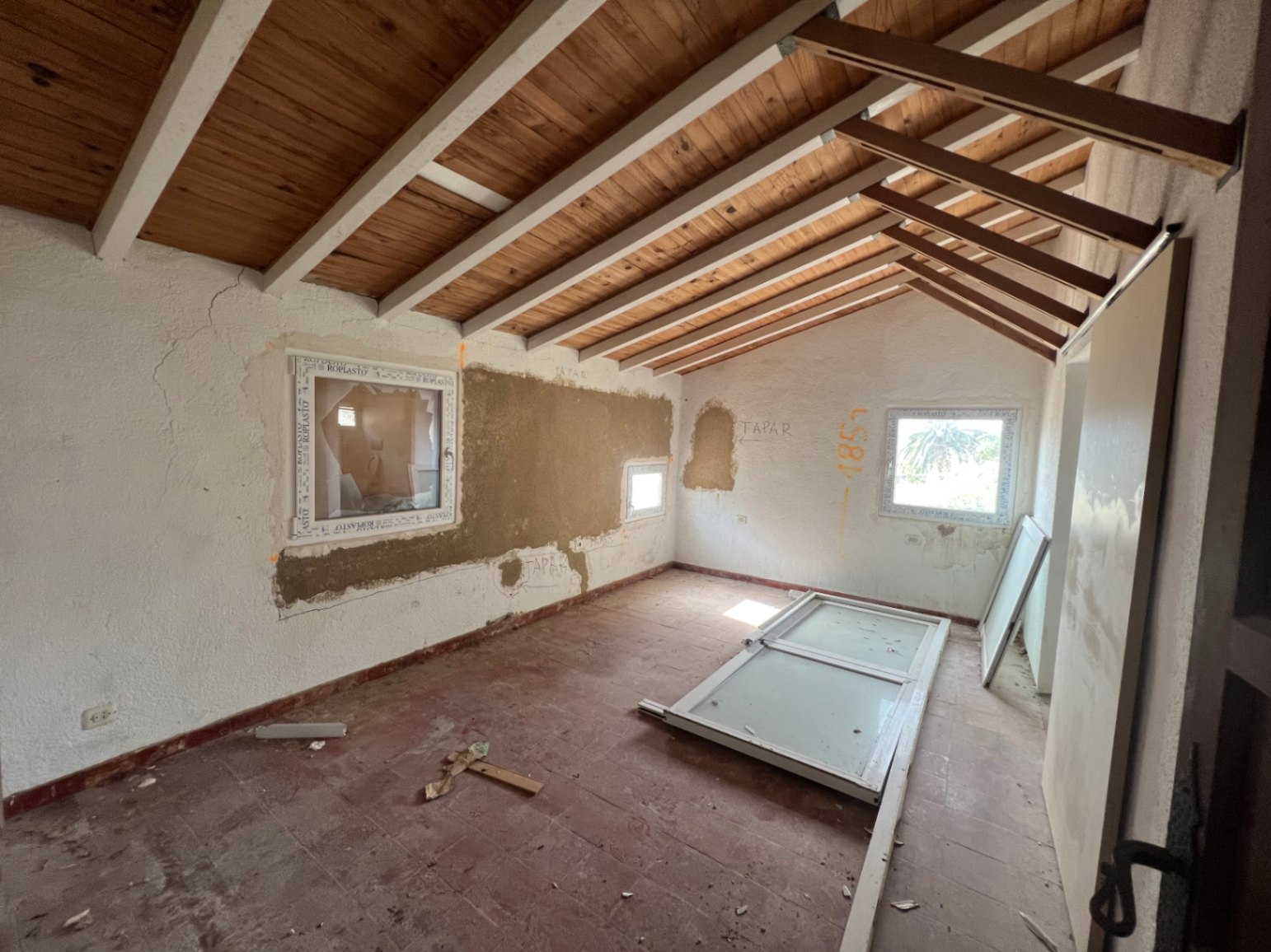 Pièce en cours de rénovation avec plafond à poutres apparentes, sol en terre cuite d'origine et nouvelles menuiseries en PVC.