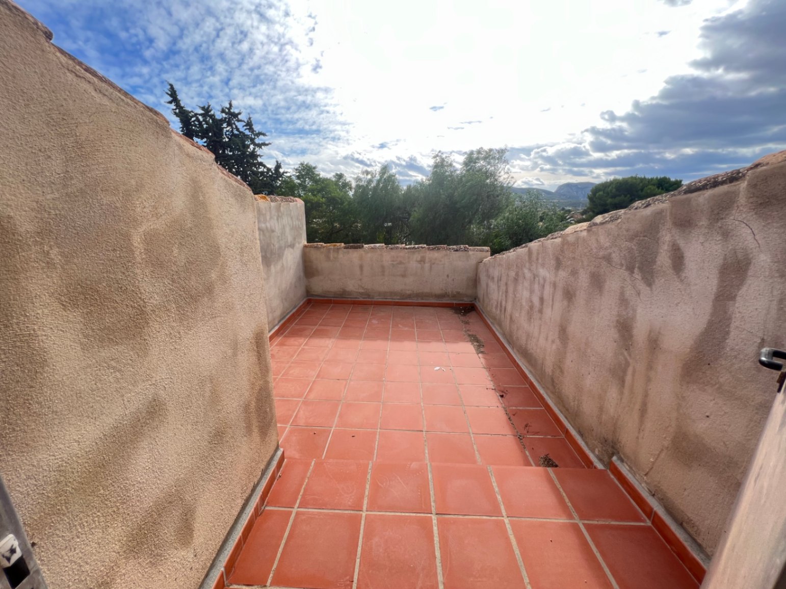 Terrasse à l'étage avec revêtement en terre cuite et hauts murs de protection, offrant une vue dégagée sur la végétation locale et les reliefs environnants.