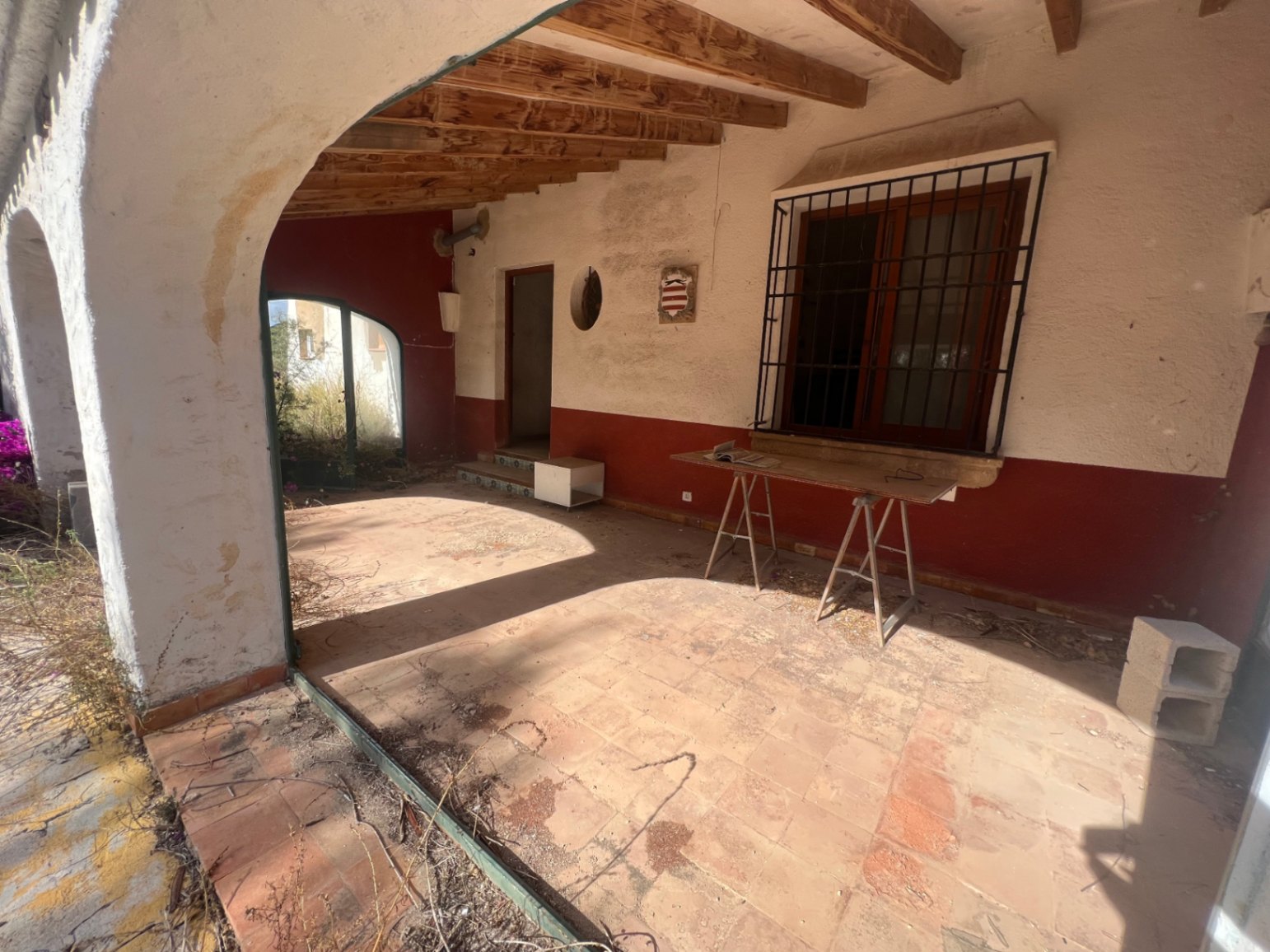 Terrasse couverte avec poutres en bois apparentes, sol en terre cuite et arches traditionnelles. Cet espace nécessite une rénovation complète pour retrouver son charme.
