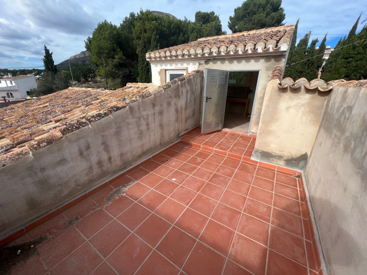 Terrasse supérieure avec revêtement en terre cuite et murets, offrant un accès à un studio indépendant sous une toiture en tuiles canal avec vue sur le Montgó.