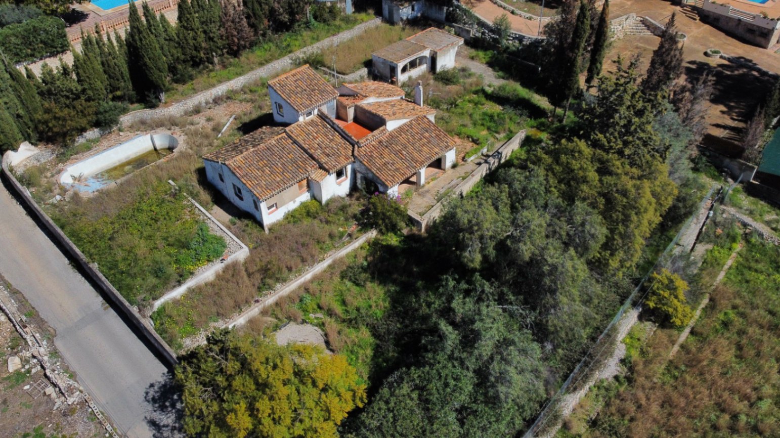 Vue aérienne de la villa révélant ses toits en tuiles, son vaste terrain arboré et la piscine à rénover, illustrant le potentiel d'agrandissement.