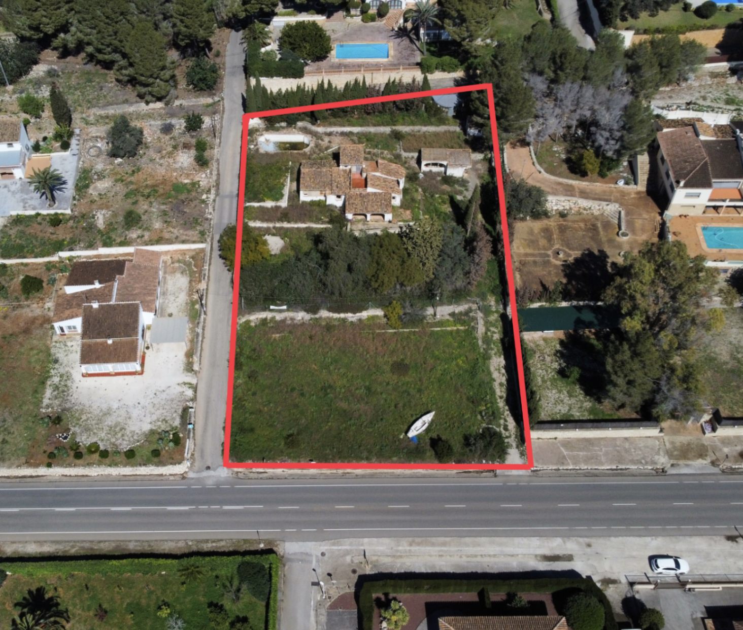 Vue aérienne délimitée du terrain de 2 895 m2 au Montgó, incluant la maison principale, les dépendances et une vaste zone de jardin avec accès direct à la route principale.