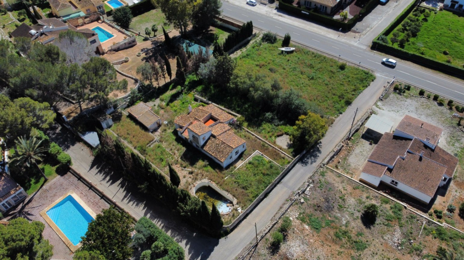 Vue aérienne du terrain de 2 895 m² à Jávea, présentant la villa aux tuiles romaines, la piscine à restaurer et la vaste parcelle arborée située dans un quartier calme.