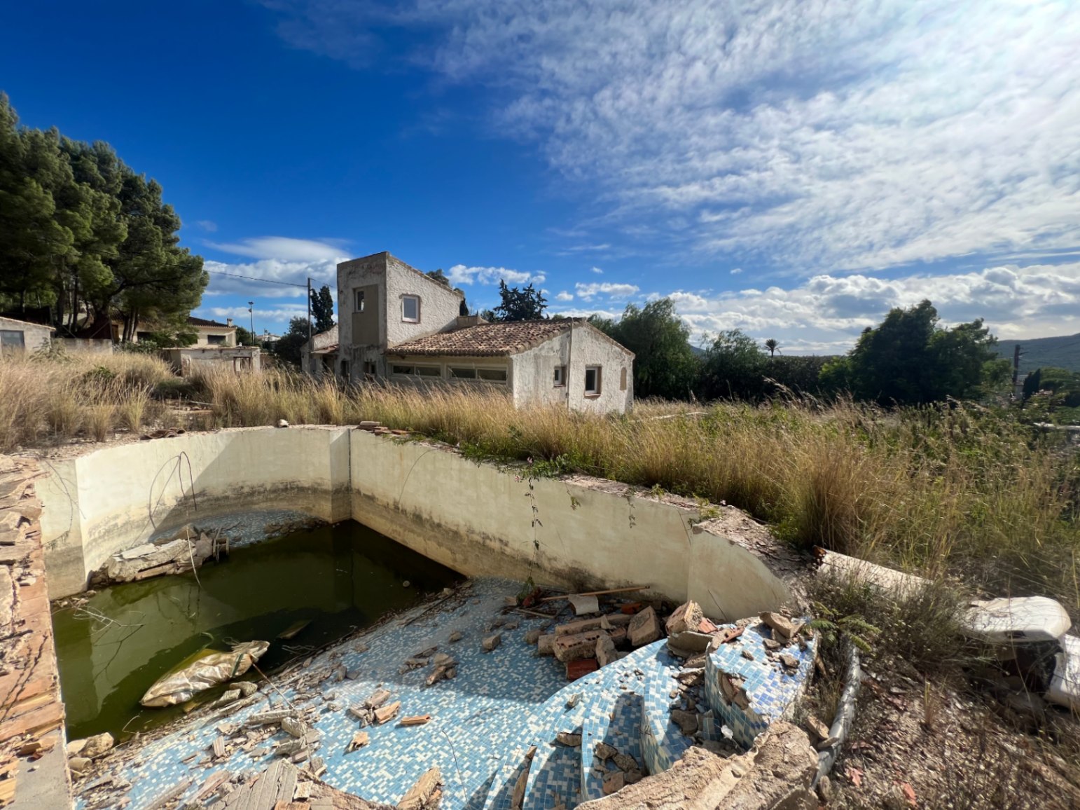 Vue extérieure de la propriété montrant la piscine à rénover et la structure de la villa traditionnelle sur un vaste terrain ensoleillé.