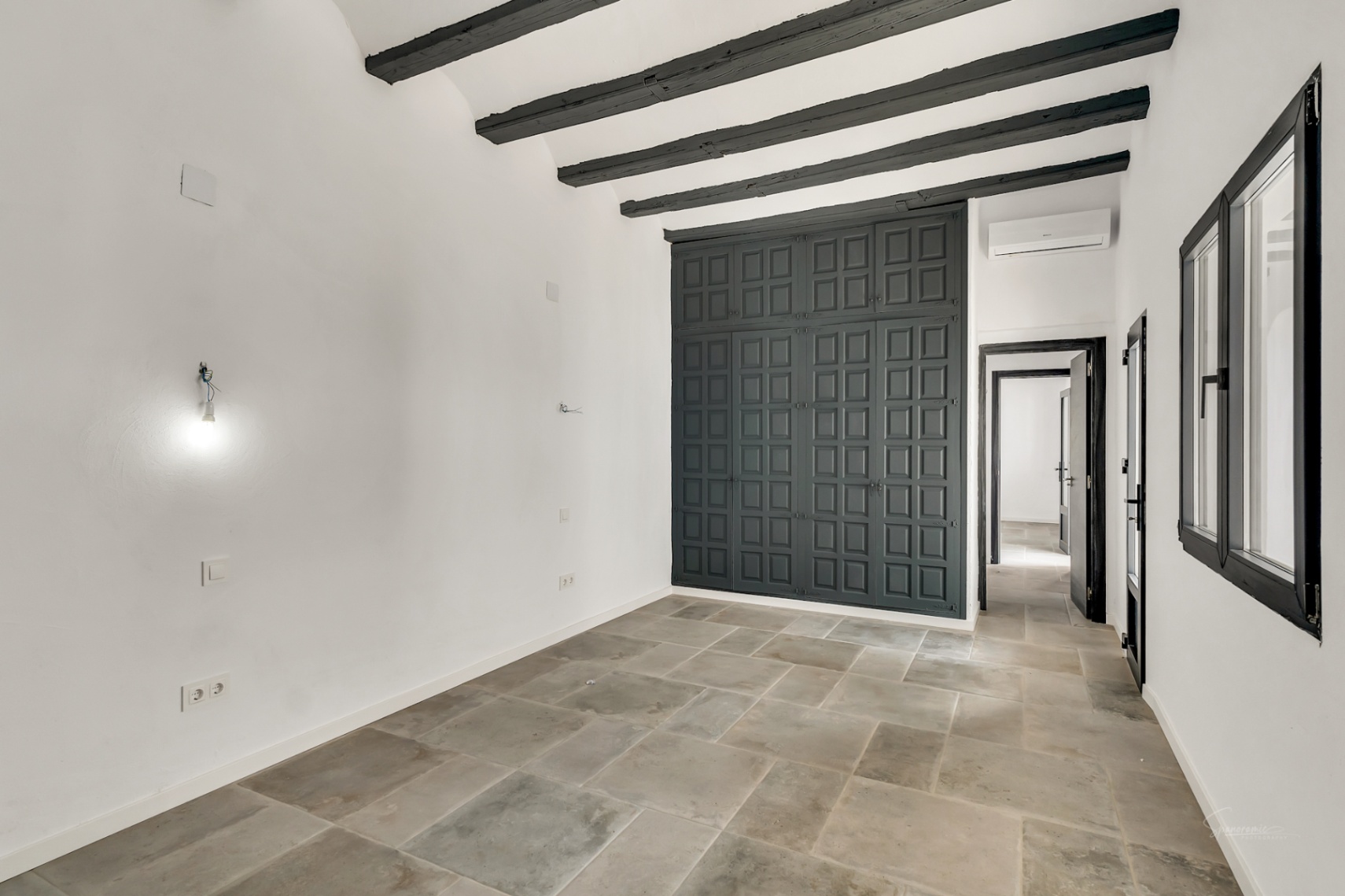Chambre avec poutres apparentes sombres, sol en pierre naturelle et une grande armoire encastrée grise au design classique et élégant.