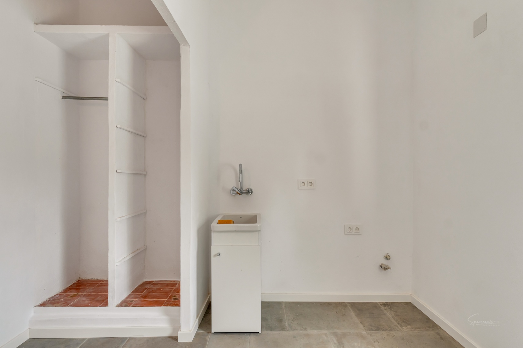 Espace buanderie avec étagères intégrées, un petit lavabo blanc et un sol en pierre grise, offrant un rangement pratique et fonctionnel.