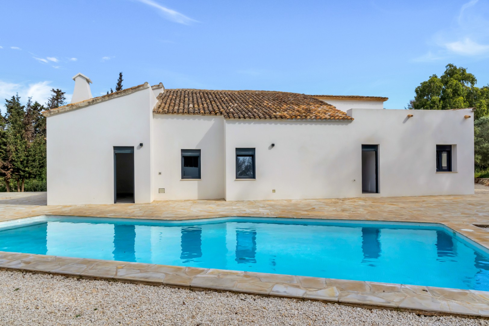 Extérieur de la villa avec piscine privée et vaste terrasse en pierre naturelle. La façade blanche et le toit en tuiles traditionnelles offrent un style méditerranéen épuré.