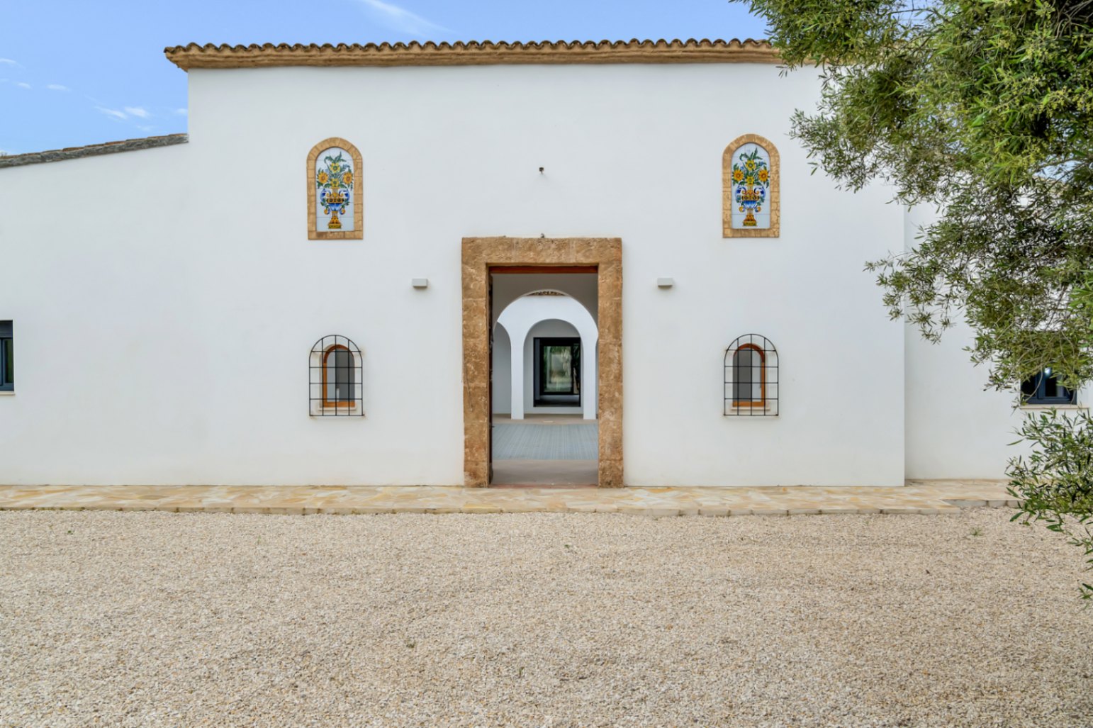 Façade méditerranéenne blanche avec entrée encadrée de pierre naturelle, panneaux de céramique décoratifs et vue sur le patio intérieur à arcades.