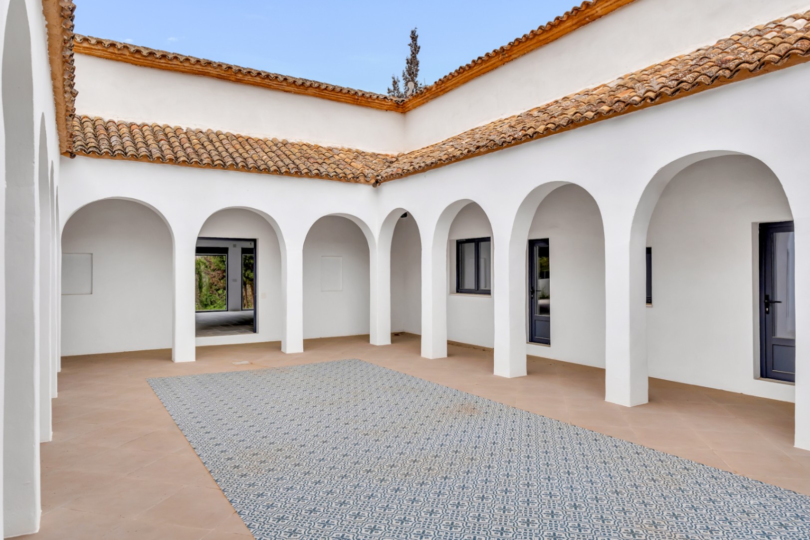 Patio intérieur central avec des arches blanches, une toiture en tuiles romaines et un sol en terre cuite orné d'un tapis de carreaux à motifs géométriques.