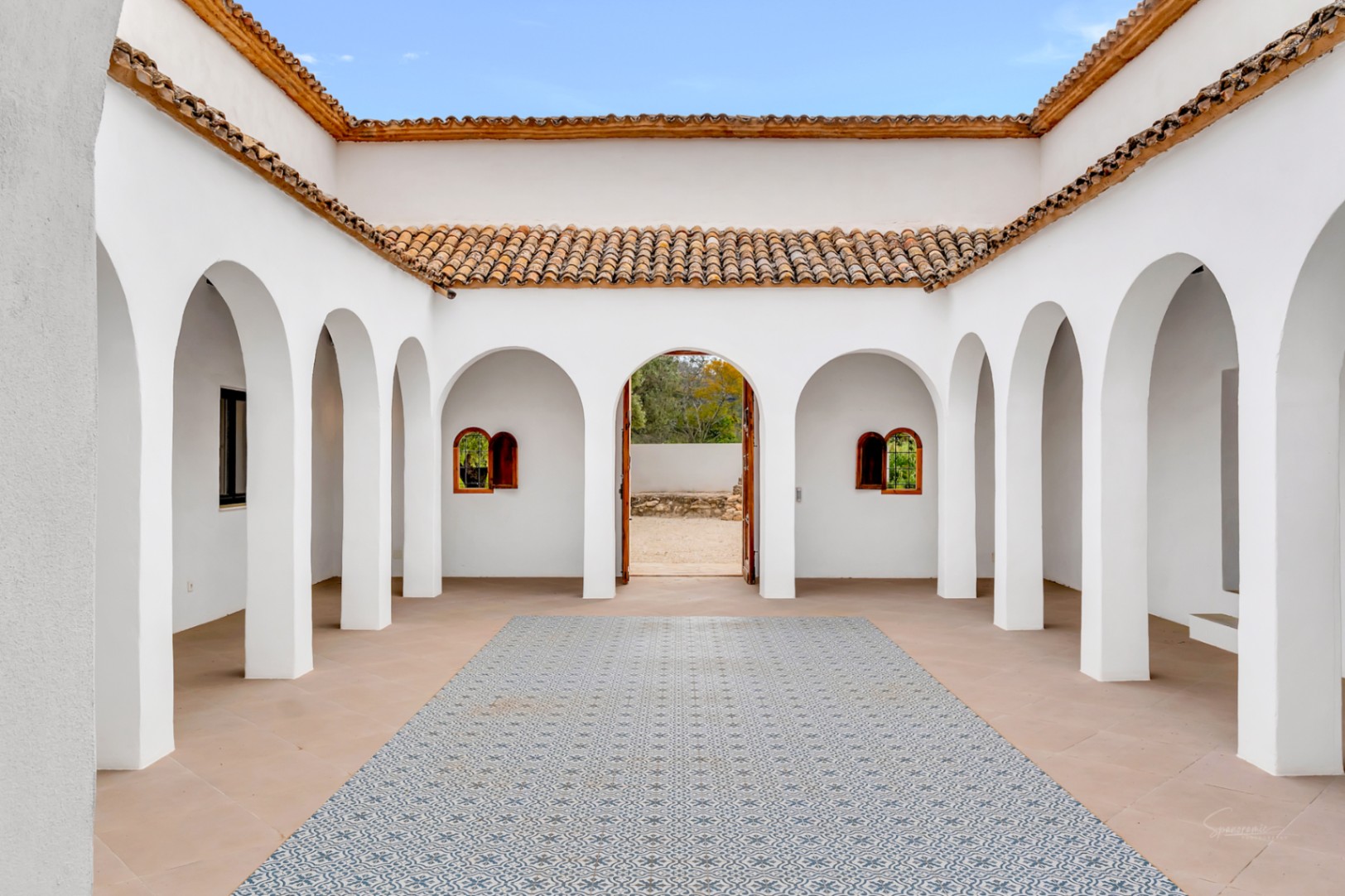 Patio intérieur de style méditerranéen avec des arcades blanches, des toits en terre cuite et un sol orné de carreaux de ciment aux motifs géométriques.