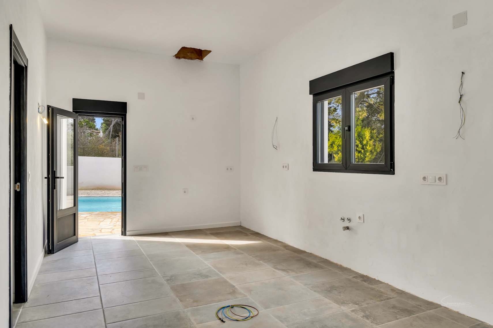 Pièce en cours de rénovation avec sol en grès, menuiseries noires et accès direct vers l'espace piscine et la terrasse.