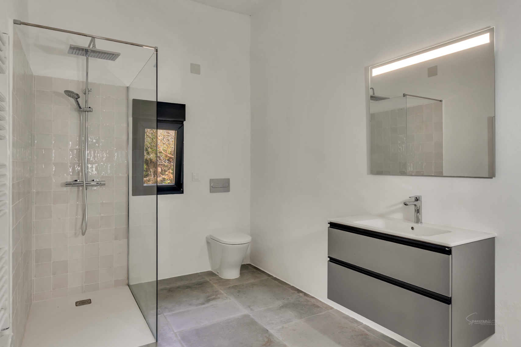 Salle de bain moderne avec douche à l'italienne, paroi en verre, WC suspendu et meuble vasque flottant gris avec miroir rétroéclairé.