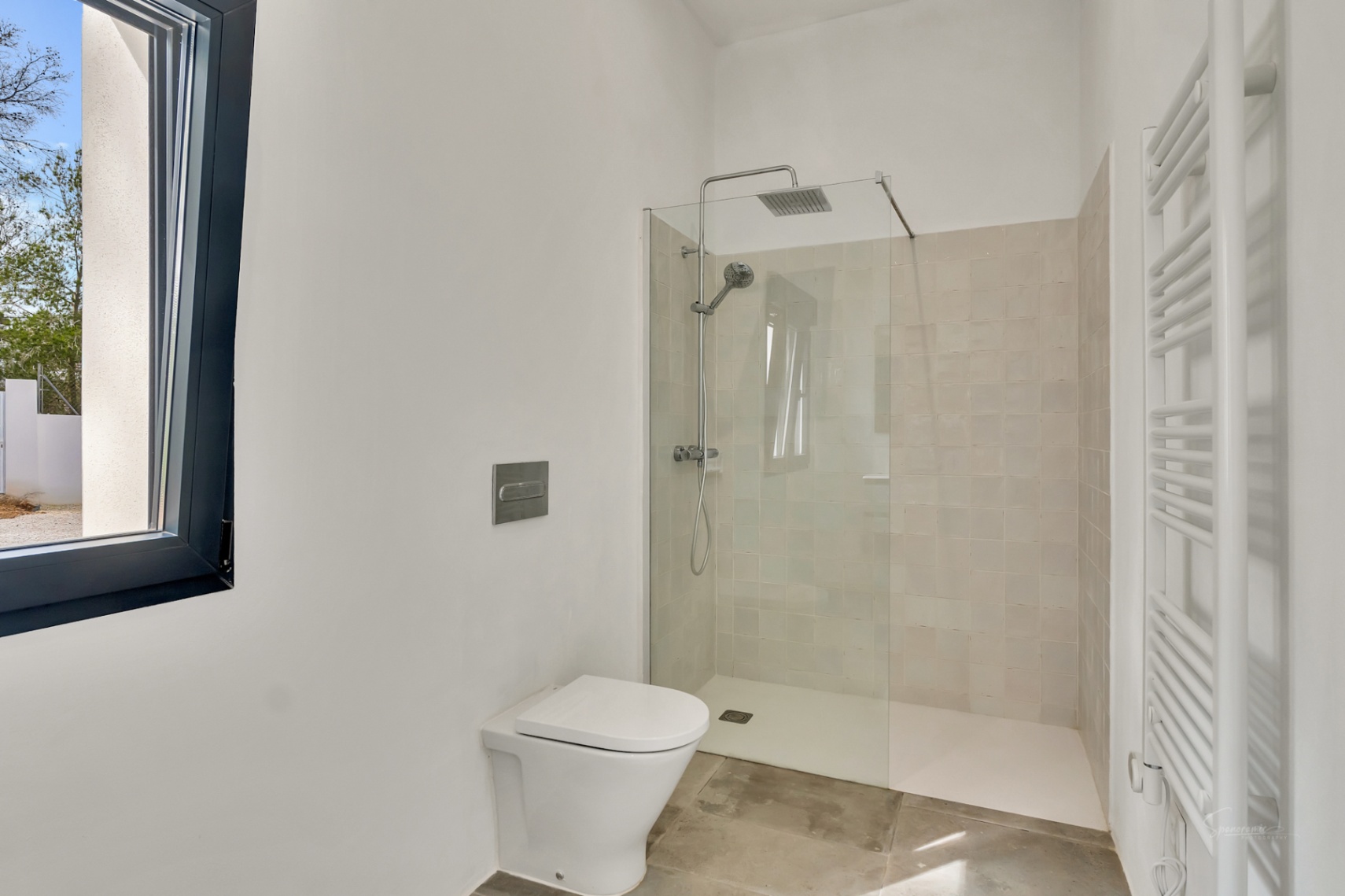 Salle de bain moderne avec douche à l'italienne, paroi en verre, WC suspendu et radiateur sèche-serviettes blanc sur fond de murs épurés et sol en pierre.