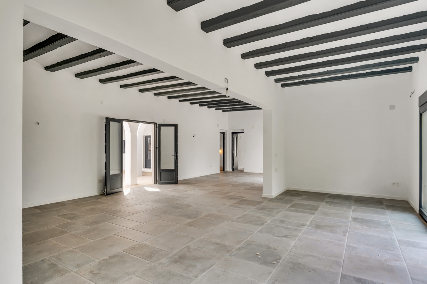 Vaste séjour décloisonné avec sol en pierre naturelle et hauts plafonds ornés de poutres en bois sombre. De grandes portes vitrées s'ouvrent sur le patio intérieur.