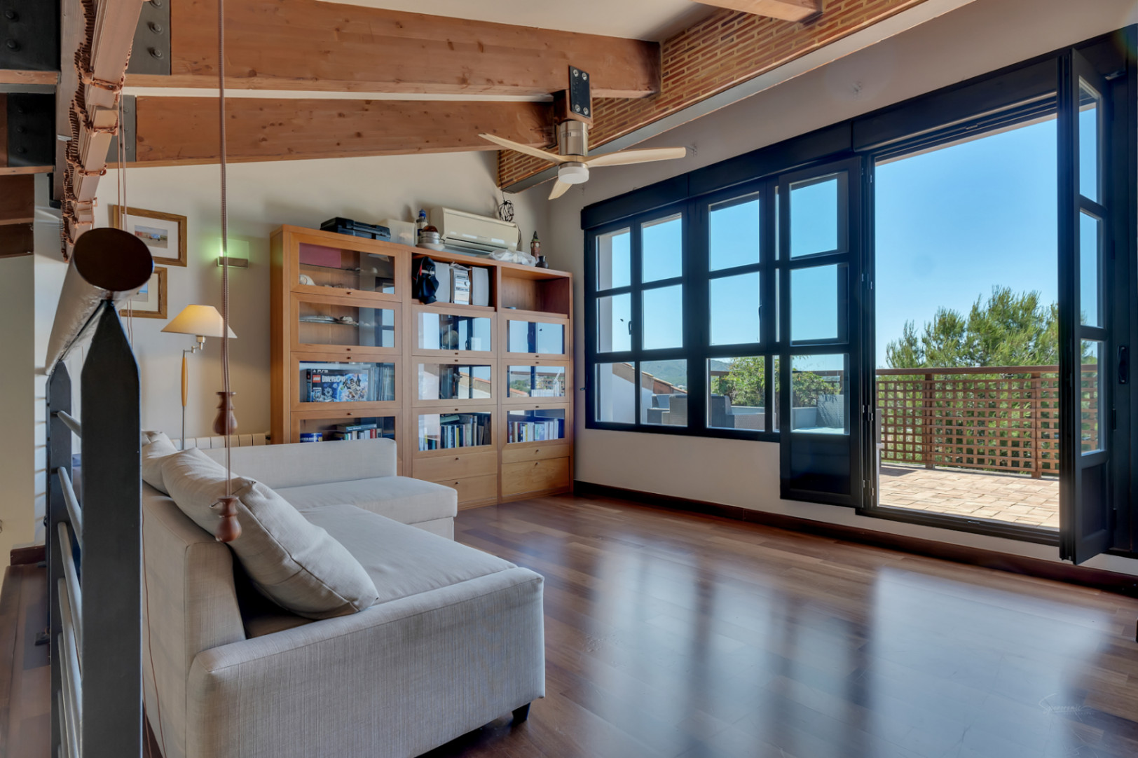 Bureau ou chambre à l'étage avec poutres en bois apparentes, parquet et grandes baies vitrées menant à une terrasse privée ensoleillée.