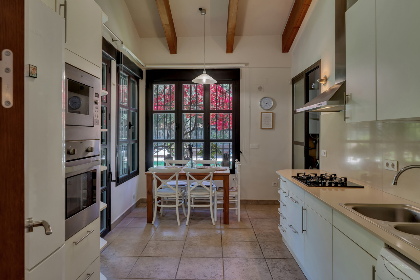 Cuisine fonctionnelle avec hauts plafonds, poutres apparentes et coin repas, dotée de grandes fenêtres offrant une vue sur le jardin et la végétation.